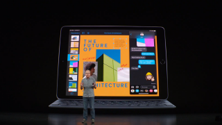 A man standing on stage with an iPad 7th Gen with keyboard attached displayed on screen behind